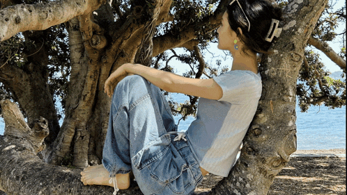 a woman is sitting on a tree branch looking at the water