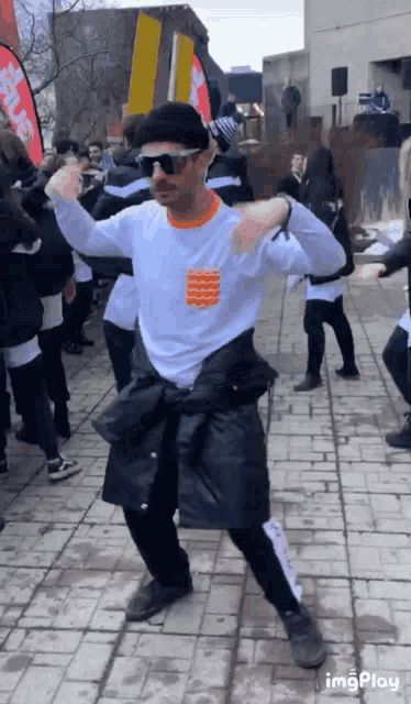 a man wearing sunglasses and a black hat is dancing in front of a crowd