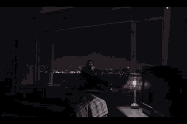 a man is sitting in front of a window looking out at a city at night