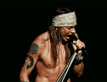 a shirtless man singing into a microphone with a bandana around his head