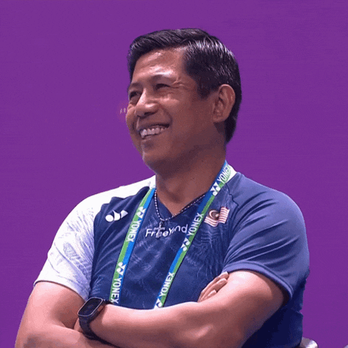 a man wearing a blue yonex shirt with a lanyard around his neck