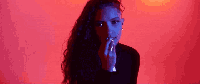 a woman is smoking a cigarette in front of a red wall .