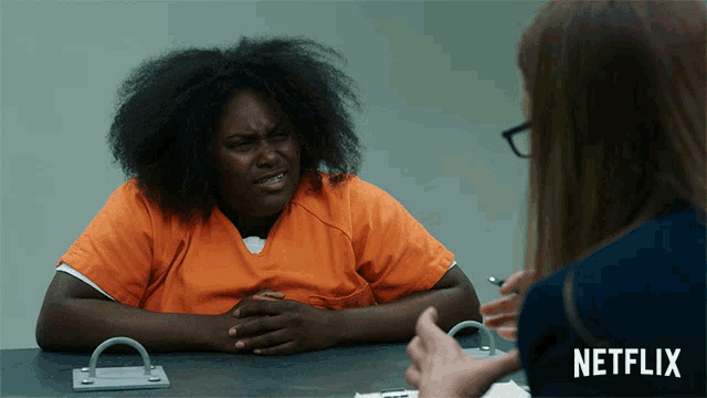 a woman in an orange uniform sits at a table with a netflix logo