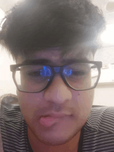 a young man wearing glasses and a striped shirt makes a funny face