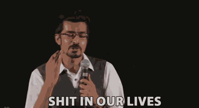 a man is holding a microphone and saying `` shit in our lives '' while standing in front of a black background .