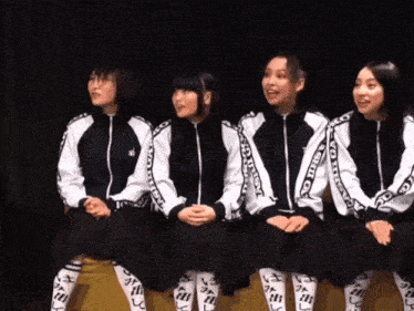 a group of girls are sitting in a row wearing black and white jackets that say tokyo