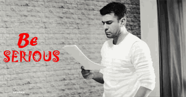 a man holding a piece of paper with the words be serious written in red