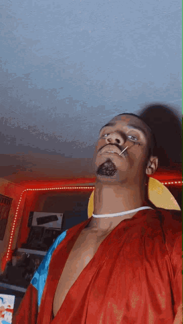 a man in a red robe is smoking a cigarette and wearing a choker around his neck