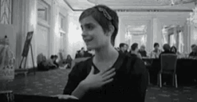 a black and white photo of a woman holding her hand to her chest in a room .