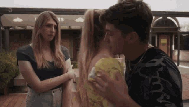 a man kisses a woman while a woman looks on