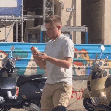 a man standing next to a vespa scooter looking at his phone