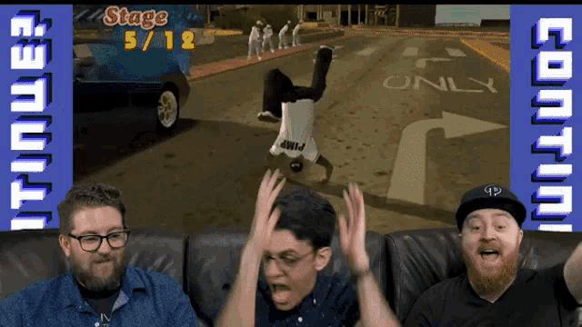 three men are sitting on a couch playing a video game with stage 5/12 written on the screen
