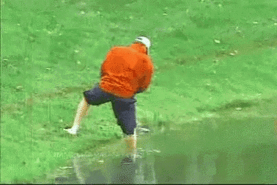 a man in an orange jacket is standing in a puddle of water on a golf course .
