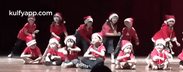 a group of children dressed in santa hats are sitting on the floor .