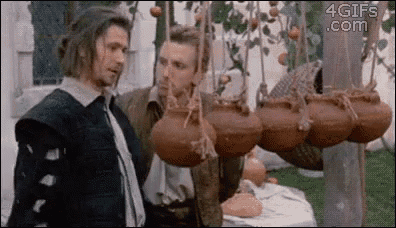 two men are standing in front of a table with pots hanging from a pole .