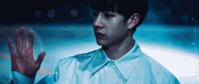 a young man in a white shirt holds his hand up