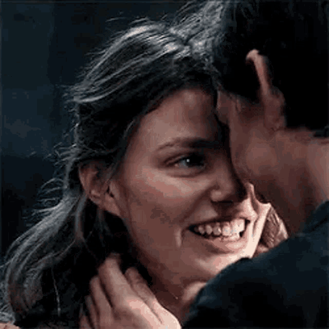 a man is touching a woman 's face while they are smiling and looking at each other .