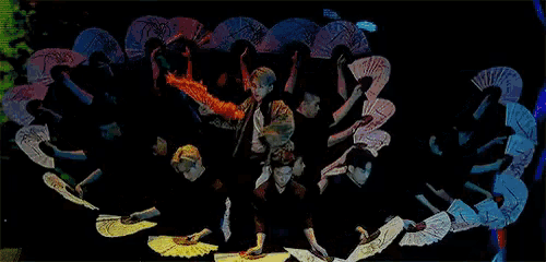 a group of people are holding fans in a circle on a stage .
