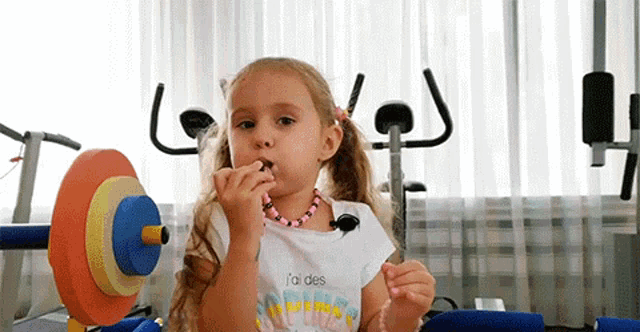 a little girl is wearing a necklace and eating a candy bar in a gym .