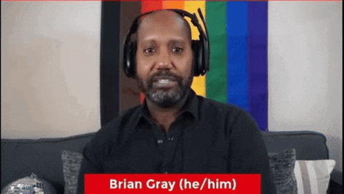 a man wearing headphones is sitting in front of a rainbow flag and says brian gray