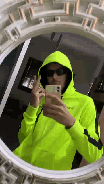 a man in a neon yellow hoodie is taking a picture of himself in the mirror .