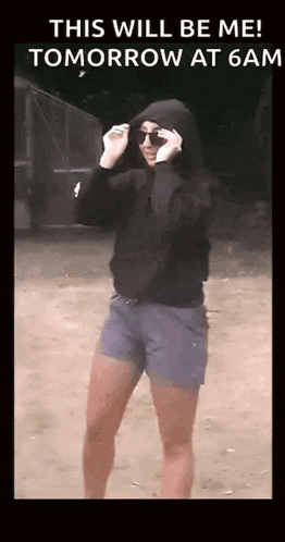 a woman wearing a hoodie and shorts is standing in the dirt .