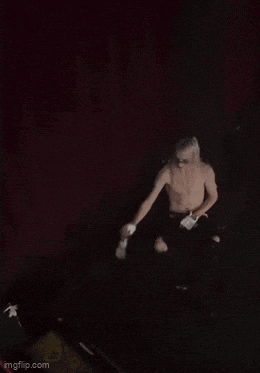 a shirtless man is dancing in a dark room with gloves on .