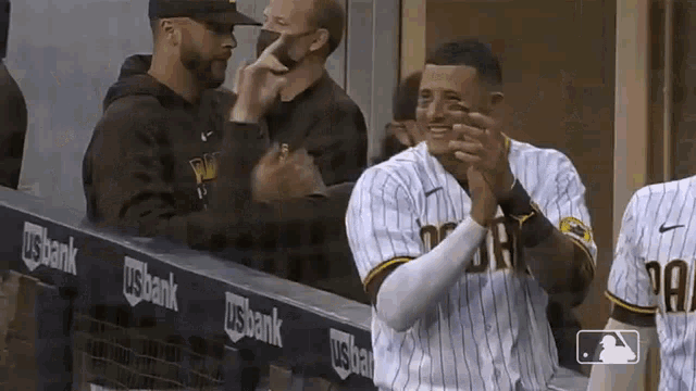 a baseball player is clapping his hands in the dugout while wearing a face mask .