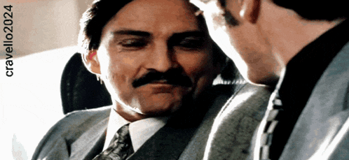 a man with a mustache is talking to another man with cravello2024 written below him