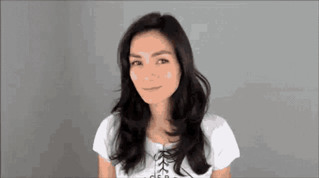 a woman with long black hair is wearing a white shirt and smiling at the camera .