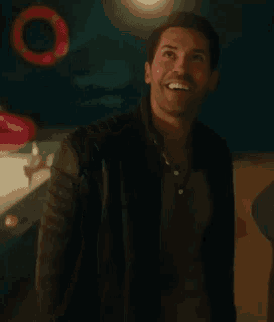 a man in a leather jacket is smiling while standing in a room .