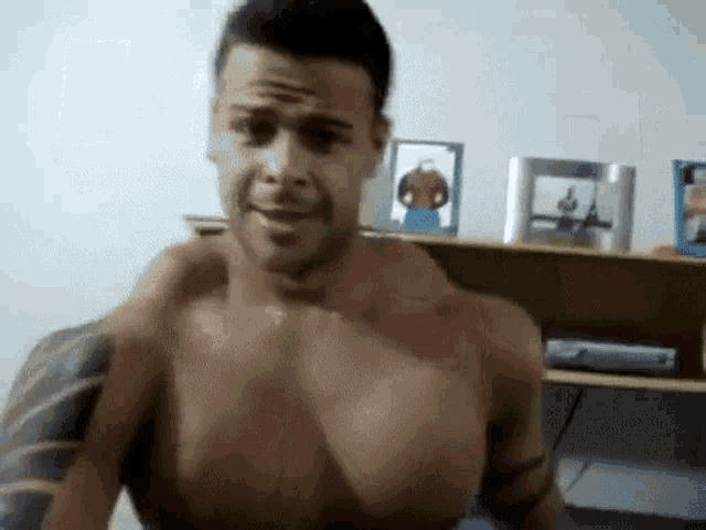 a shirtless man with tattoos on his arms is standing in front of a shelf .
