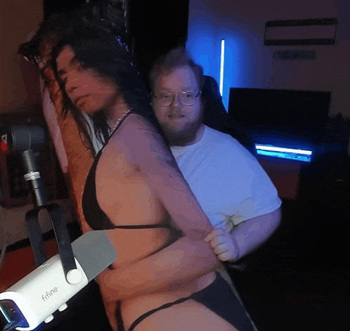 a woman in a bikini is being held by a man with glasses and a camera that says ' ffine ' on it