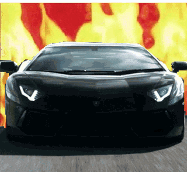a black lamborghini is driving in front of a fire background