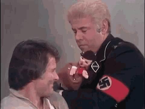 a man in a nazi uniform is holding a doll and talking to a man .
