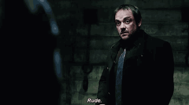 a man in a suit and tie says " rude " in a dark room