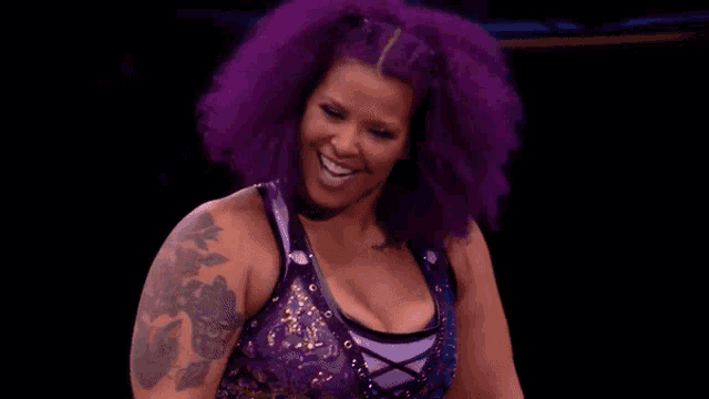 a woman with purple hair and a tattoo on her arm is making a peace sign .