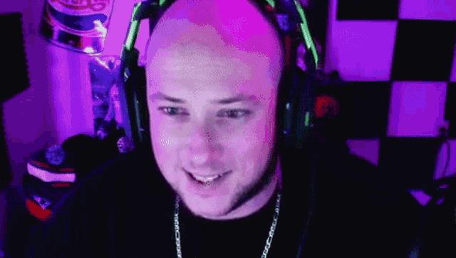 a bald man wearing headphones is smiling and looking at the camera in a purple room .