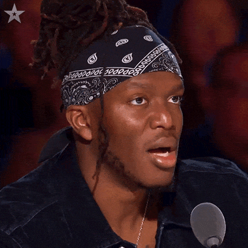a man with dreadlocks and a bandana on his head says whoa in front of a microphone