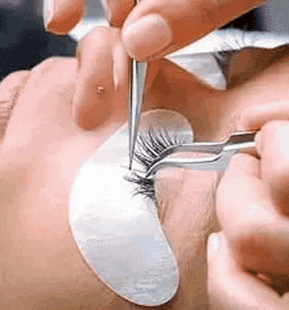 a close up of a person applying eyelashes with tweezers .