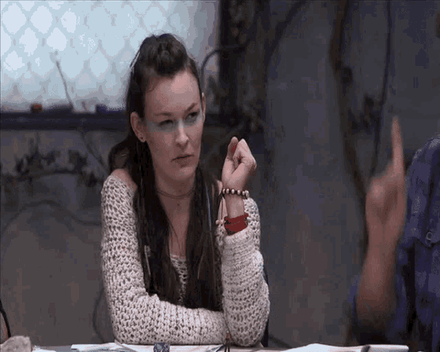 a woman with dreadlocks is sitting at a table with a man pointing at her