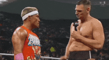 two men are standing next to each other in a wrestling ring talking to each other .
