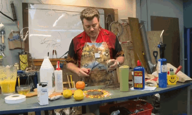 a man in a red shirt is standing in front of a table with bottles of glue and a smiley face mug