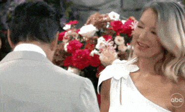a man and a woman are standing in front of a bouquet of red and white flowers .