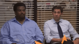 two men are sitting next to each other in front of a window in an office .