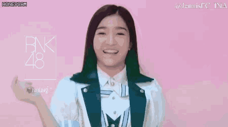 a girl is smiling and holding her fist in the air while wearing a jacket and a white shirt .