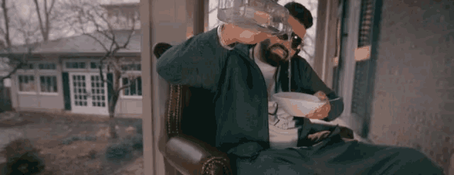 a man with a beard is sitting in a chair drinking milk from a bottle .