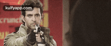 a man is holding a gun in front of a red sign that says kulfyapp.com .