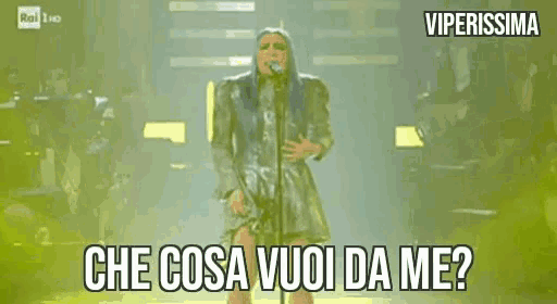 a woman is singing into a microphone on a stage and the words che cosa vuoi da me are on the screen .