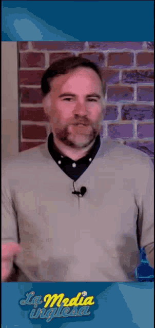 a man with a beard is standing in front of a brick wall with a microphone on his neck .